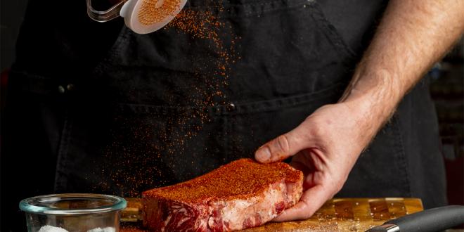 a man sprinkling dry rub on a strip steak