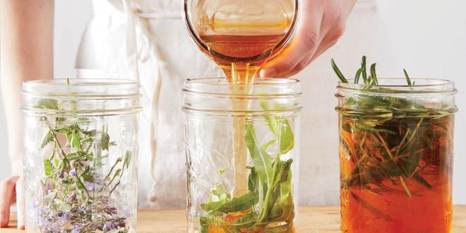 A woman in a white apron pouring honey into jars of herbs.