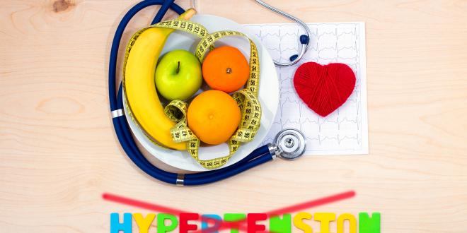 A bowl of fruit, measuring tape, and a stethoscope on a cardiac chart