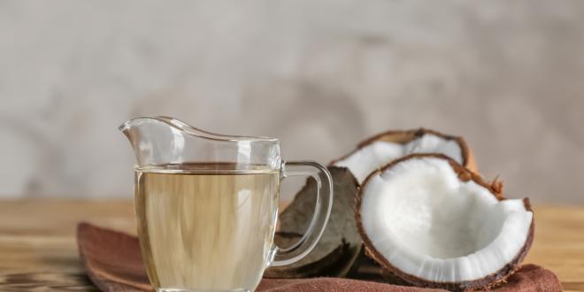 Ripe coconut and pitcher with MCT oil on a wooden table.