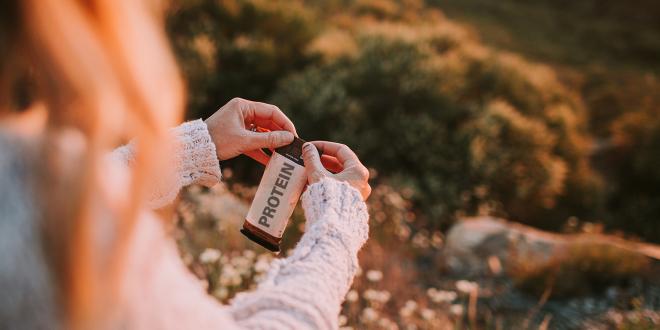 A hiker opening a protein bar