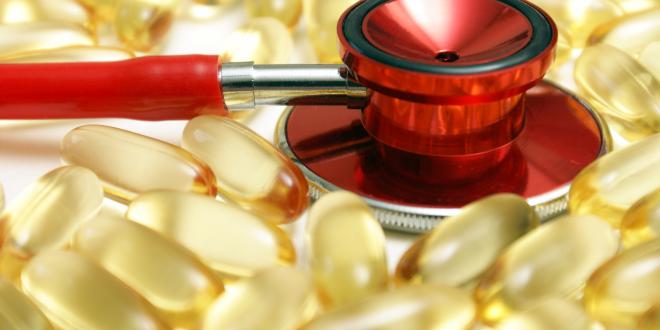 Red stethoscope resting on omega 3 capsules.