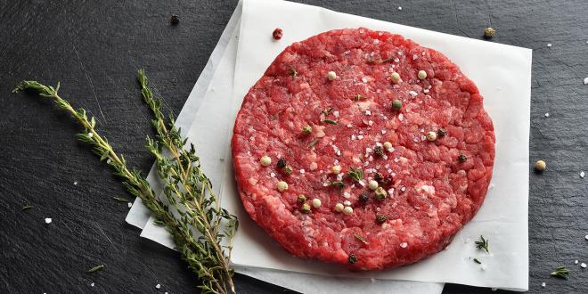 a seasoned burger patty ready to grill