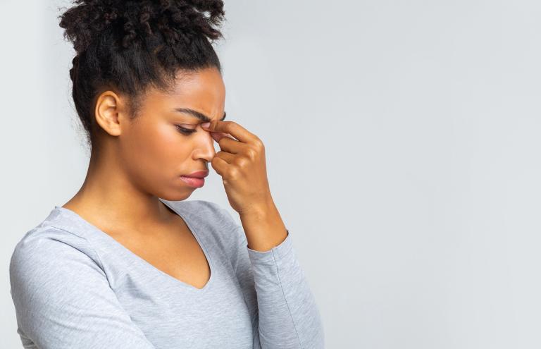 a young woman holding the bridge of her nose due to sinus pain